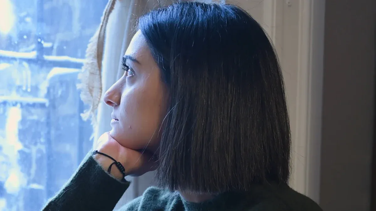 Silhouette of a woman with black straight hair looking out a window on a cloudy day, showcasing industrial workwear apparel.