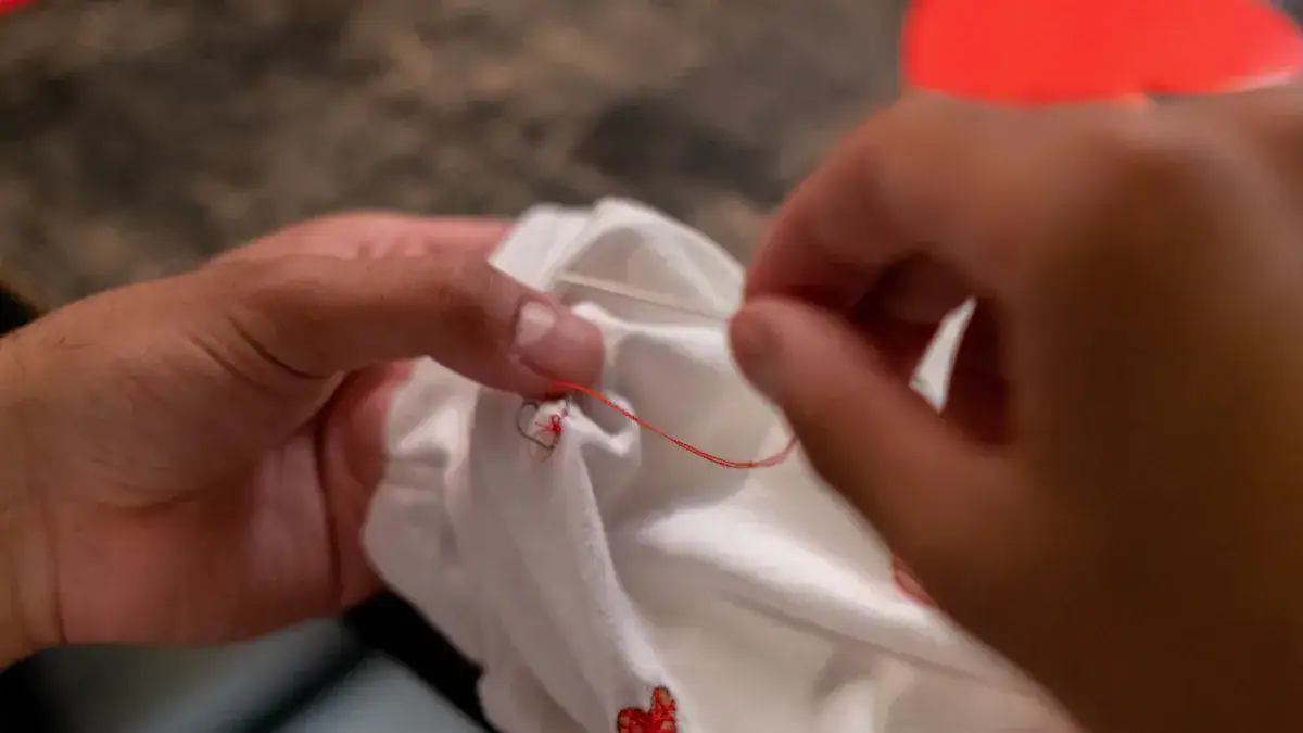 Bright white uniform fabric being carefully stitched with red thread, showcasing custom clothing manufacturing and embroidery craftsmanship.