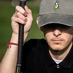 Stylish golfer wearing custom golf apparel and cap, holding a golf club outdoors on a sunny day.