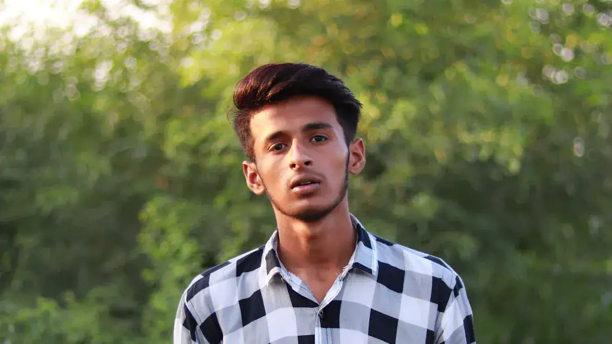 Young man wearing a custom checked shirt outdoors on green foliage background.