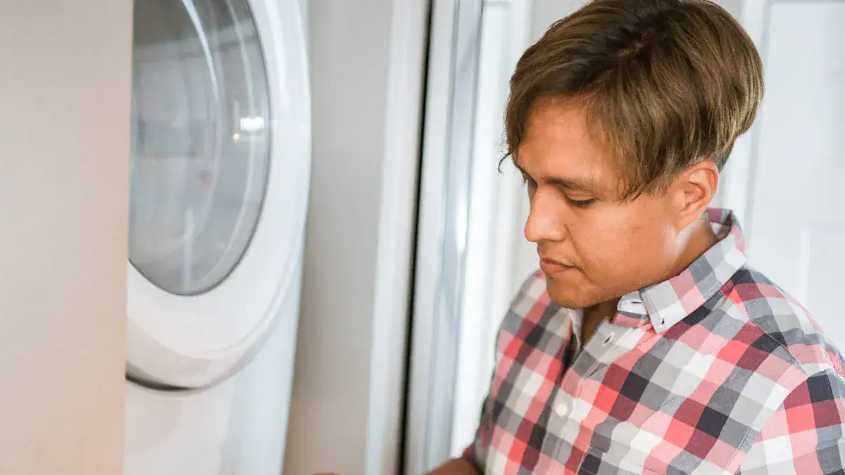 Efficient laundry worker in a checkered uniform using washing machine for commercial clothing cleaning.