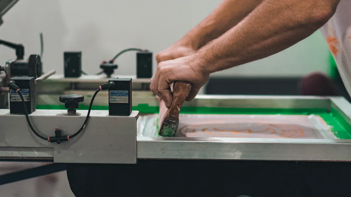 Brightly colored screen printing process on fabric for custom workwear uniforms at a Chinese manufacturing facility. Hands of a worker skillfully operate printing machine to create high-quality uniforms.