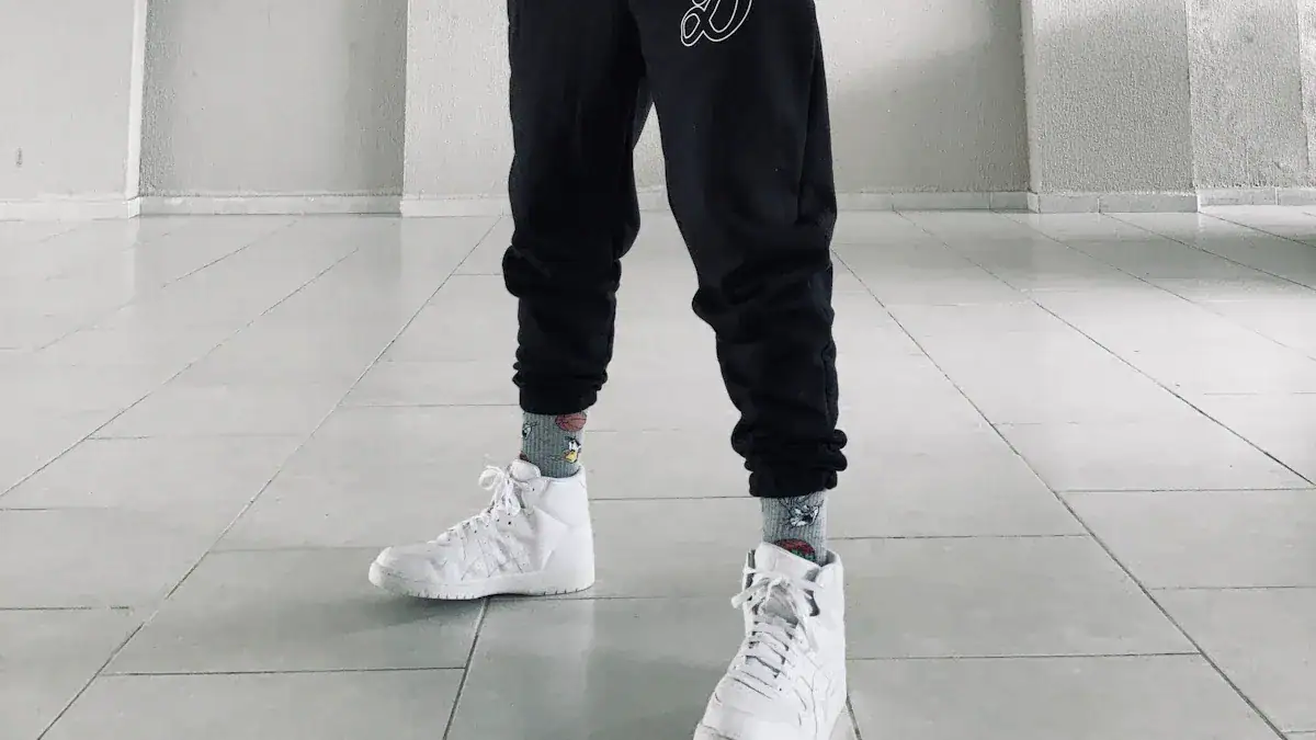 Bright white sneakers paired with black joggers and colorful patterned socks, showcased on a minimalistic tiled floor, highlighting trendy casual footwear and apparel styling.