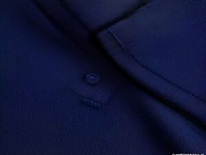 Close-up of navy polo collar, placket, pocket, buttons, and fabric texture.